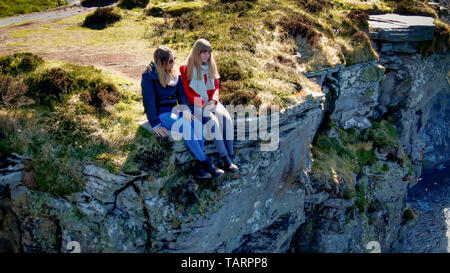 Deux jeunes filles s'asseoir sur le bord de les célèbres falaises de Moher en Irlande - photos de voyage Banque D'Images