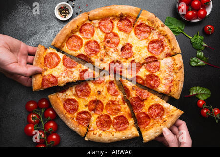 Pizza au pepperoni, sur fond de béton noir vue d'en haut. Les personnes prenant Tranche de pizza. Cuisine de fête, de mauvaise alimentation concept Banque D'Images