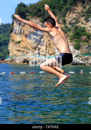 Brave adolescent saute d'une falaise dans la mer sur la toile de bouées côtes défensives Banque D'Images