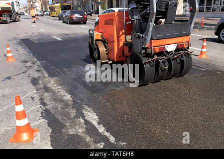 Une patinoire vibratoire lourd est la réparation d'une section de la route clôturée par des cônes de circulation sur une rue de la ville. Banque D'Images