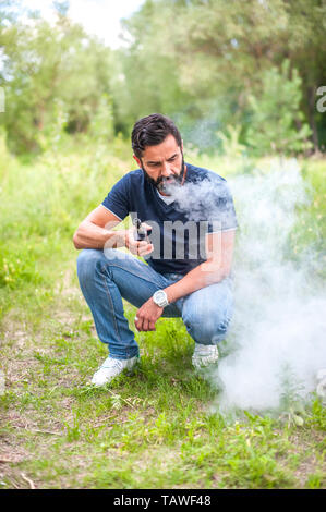 Homme Confidentvape fumer une cigarette électronique dans la nature. Concept de santé. Banque D'Images