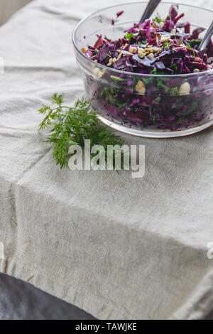 Salade de chou bleu frais avec les herbes et les noix dans un bol en verre sur une nappe rustique. Verser sur la sauce. Concept d'aliments sains et nutritifs Banque D'Images