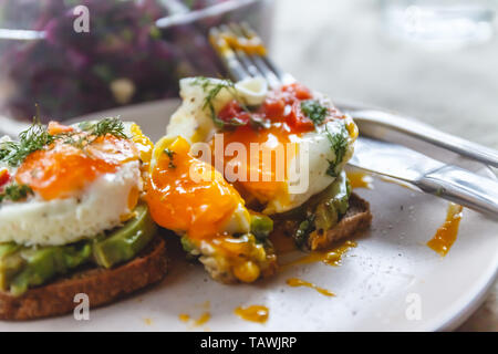 Petit déjeuner servi de deux toasts avec l'avocat, oeufs au plat avec légumes et fines herbes sur une nappe rustique arrière-plan. Vue de dessus. En bonne santé et nutr Banque D'Images