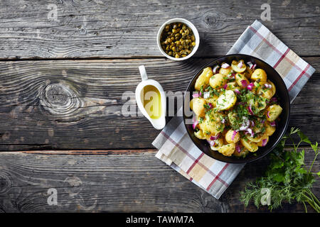 Délicieuses nouvelles salade de pommes de terre avec l'oignon rouge, les câpres, les verts dans un bol la moutarde noire. de vinaigre et les câpres sur une vieille table rustique en bois, horizont Banque D'Images