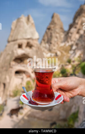 La main de femme tenant un verre de thé turc traditionnel avec le célèbre château d'Uchisar à contexte en Cappadoce Banque D'Images