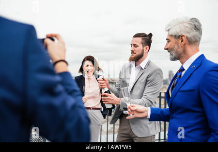 Un groupe de joyeux businesspeople having a party en plein air sur la terrasse du toit en ville. Banque D'Images