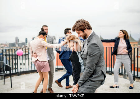 Un groupe de joyeux businesspeople having a party en plein air sur la terrasse du toit dans la ville, la danse. Banque D'Images