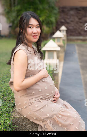 Belle asiatique femme enceinte au repos dans l'arrière-plan le jardin. Banque D'Images