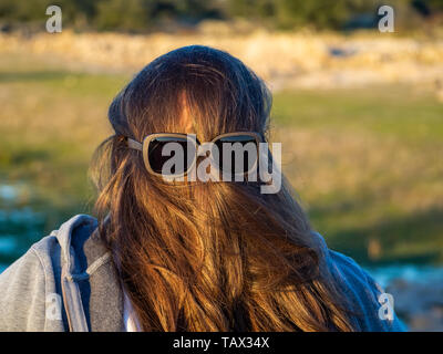 Une femme curvy making des gestes avec les cheveux en face de son visage et des lunettes de soleil Banque D'Images
