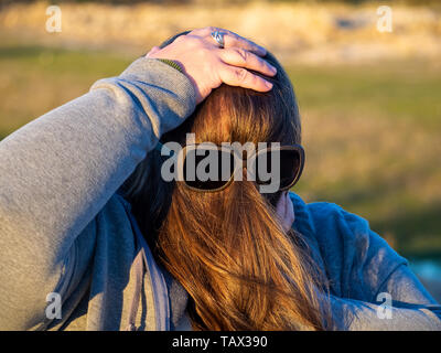 Une femme curvy making des gestes avec les cheveux en face de son visage et des lunettes de soleil Banque D'Images