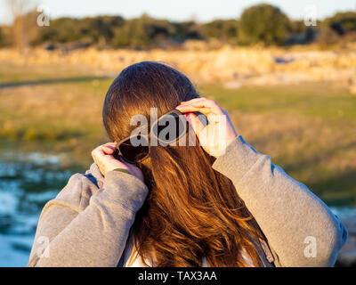 Une femme curvy making des gestes avec les cheveux en face de son visage et des lunettes de soleil Banque D'Images