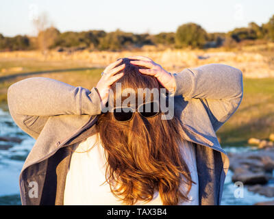 Une femme curvy making des gestes avec les cheveux en face de son visage et des lunettes de soleil Banque D'Images