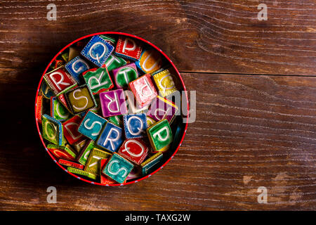 Tin Can plein de carreaux de céramique colorés avec des lettres sur la texture du bois Banque D'Images