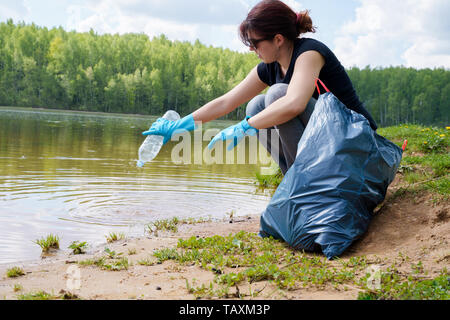 Image de la femme dans les gants en caoutchouc avec une bouteille de plastique sale dans ses mains sur les bords de la rivière Banque D'Images