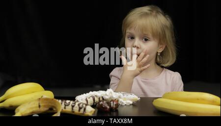 Beau, heureux enfant consomme du sirop de chocolat fondu et de crème fouettée sur fond noir. Teen blonde girl in pink shirt. Cute smiling. Visage sale Banque D'Images