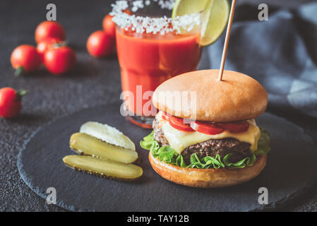 Hamburger avec un verre de jus de tomates sur le bord de la pierre noire Banque D'Images