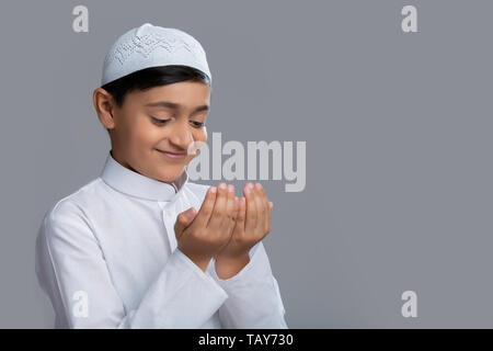 Jeune garçon musulman wearing cap priant et souriant Banque D'Images