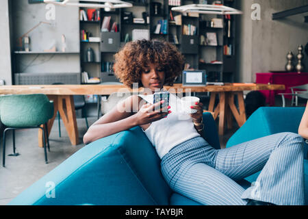 Jeune femme noire de boire et bavarder avec smartphone dans loft moderne - jeunes, gai, plein de Banque D'Images