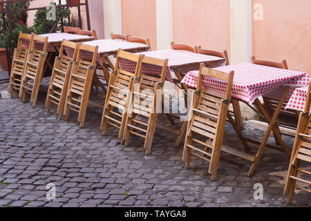 Gros plan vue perspective de rue Italien traditionnel restaurant terrasse avec des tables couvertes de tissu à carreaux et des chaises en bois sur de vieux trottoir Banque D'Images