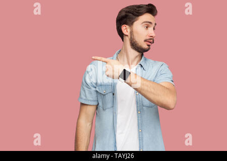 Sortir d'ici. Portrait de beau jeune homme barbu en colère en bleu style casual shirt debout et montrant à côté de la sortie chemin. Piscine studio shot, je Banque D'Images