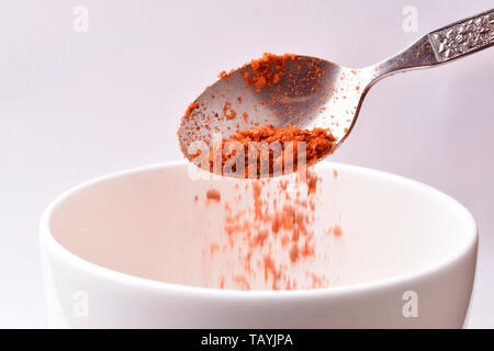 Cuillère en acier de red chili en poudre dans un bol blanc isolé sur fond blanc - Image Banque D'Images
