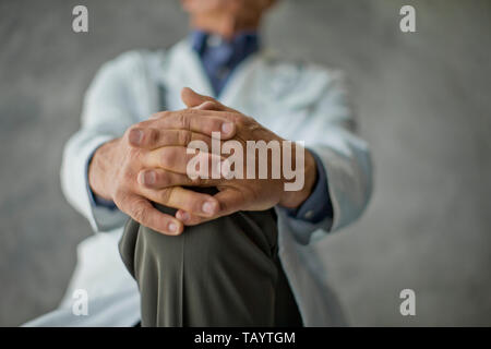 Mains d'un médecin senior agrippant son genou. Banque D'Images