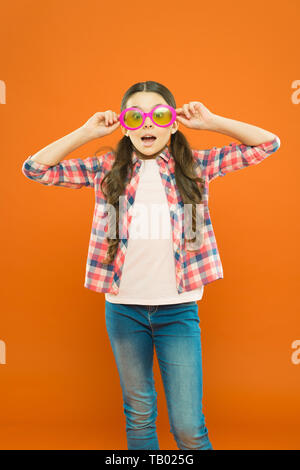 Aint cela drôle. Petite fille à lunettes avec drôle à travers le filtre de couleur sur fond orange. Enfant drôle portant des lunettes de soleil sur le visage surpris. Mes yeux rendez-vous drôle. Banque D'Images