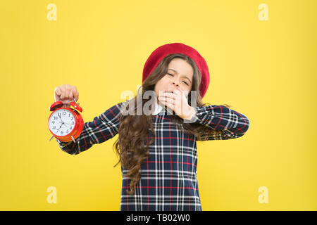 Son temps d'aller dormir. Petite fille endormie dans la soirée sur fond jaune. Le bâillement petit enfant tenant un réveil. La fin de l'époque. Temps de pause, de vous rafraîchir. Banque D'Images