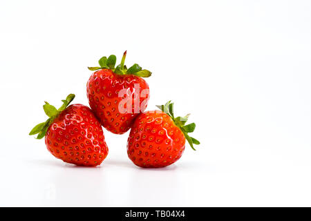 Close up de trois fraises mûres en équilibre sur l'autre. Tous sont isolés sur un fond blanc avec espace pour copier sur la gauche. Banque D'Images