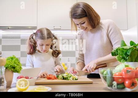 Repas cuisine maison saine par famille. Mère et fille légumes coupés à la maison dans la cuisine pour la salade. Radis rouge coupe femme, coupe fille ville énorme Banque D'Images