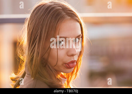 Belle adolescente européenne montre la langue, Close up portrait en extérieur avec la lumière du soleil rétro-éclairé Banque D'Images