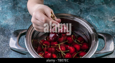 Bannière alimentaire. La main de l'enfant est titulaire de cerises douces mûres. Sweet Cherry dans une casserole sur un fond de béton bleu. Banque D'Images