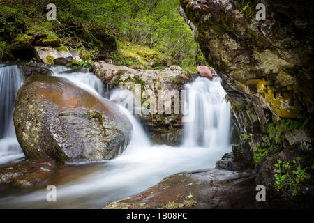 Scenic, belles cascades de petite cascade sur un ruisseau de montagne, encadrée par des falaises couvertes de mousse, avec d'énormes, d'un rocher au premier plan Banque D'Images