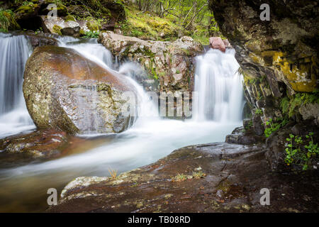 Scenic, belles cascades de petite cascade sur un ruisseau de montagne, encadrée par des falaises couvertes de mousse, avec d'énormes, d'un rocher au premier plan Banque D'Images