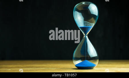 L'horloge de sable sur table en bois et fond noir. Copie de l'espace pour votre texte. Le concept du temps passé. Banque D'Images