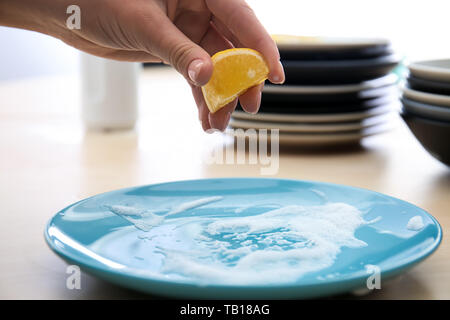 Woman squeezing jus de citron sur la plaque avec de la mousse pour le nettoyer Banque D'Images