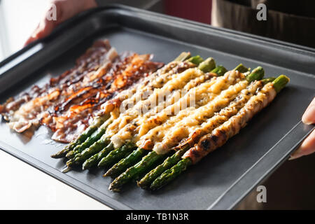 Femme tenant la plaque de cuisson avec des délicieuses asperges enveloppé de bacon Banque D'Images