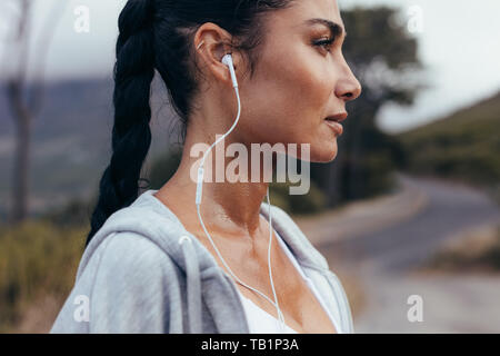 Vue latérale d'une athlète féminine wearing earphones regardant ailleurs. Femme en faisant une pause après l'extérieur de l'exercice dans matin. Banque D'Images