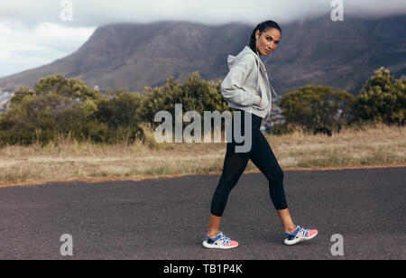 Toute la longueur de jeune femme dans les vêtements de sport marche sur route en matinée. Femme sport sur matin à pied. Banque D'Images