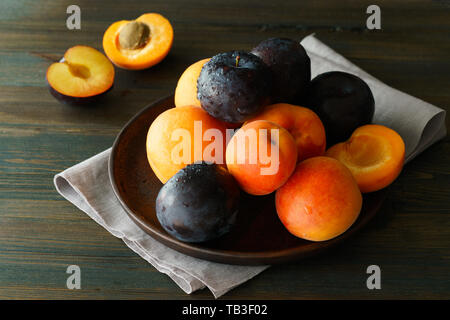 Une pile de prunes et abricots fraîchement cueillis sur une plaque de bois. Table en bois foncé, gris , haute résolution, serviette Banque D'Images