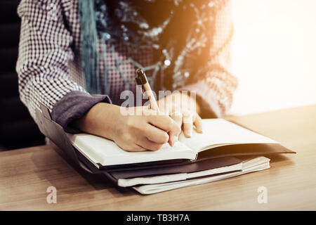 La main de femme musulmane avec l'écriture de certains remarque sur anotebook par stylo dans la matinée Banque D'Images