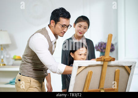 Petite fille asiatique faire une peinture obtenez de l'aide de père mère tout en regardant en arrière-plan Banque D'Images