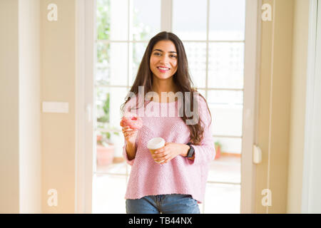 Jeune travailleur woman eating donut rose savoureux et de boire une tasse de café Banque D'Images