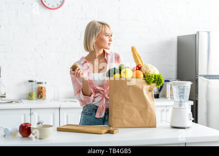 Attractive blonde woman holding kiwi près de sac de papier avec des provisions Banque D'Images