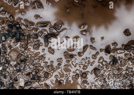 Sale flaque de boue avec de petites pierres de gravier à la lumière du jour Banque D'Images