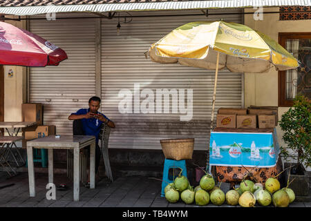 Banjar Gelulung, Bali, Indonésie - 26 Février 2019 : vendeur de rue de coco sous les parasols et de ses fruits dans cette rue Ji. Raya Sukawati. Banque D'Images