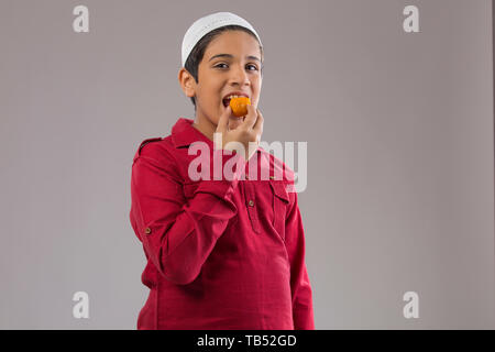 Jeune garçon musulman wearing cap de manger des sucreries Banque D'Images