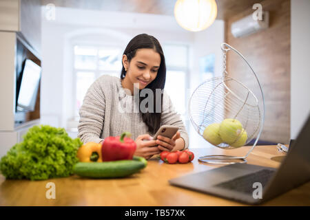 Image of caucasian woman using mobile phone pendant la cuisson des légumes frais en salade cuisine Banque D'Images