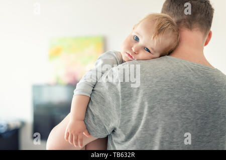 Portrait en gros plan d'un adorable garçon blanc cacheté sur l'épaule des pères à l'intérieur. Un enfant doux se sent en sécurité sur la main de daddys Banque D'Images