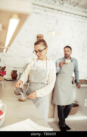 La préparation du café. Smiling barista pouring lait cuit à la belle dans une tasse de café. Banque D'Images